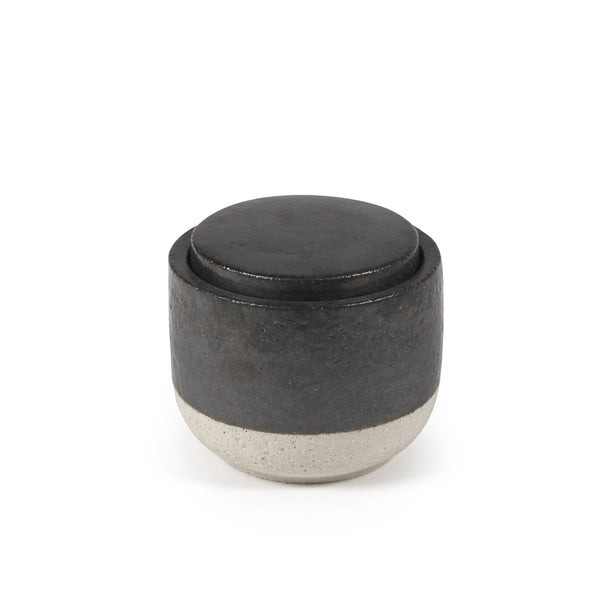 Vela perfumada decorativa en recipiente cilíndrico oscuro con tapa redonda negra