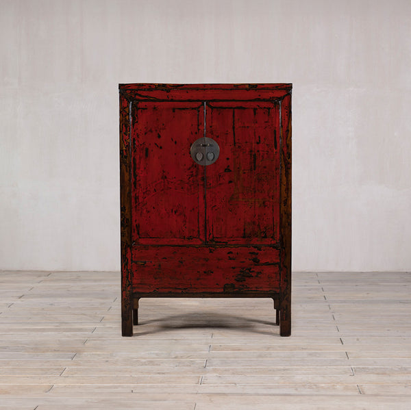 Armario antiguo de madera rojo, con una puerta y pomo circular, patas de soporte