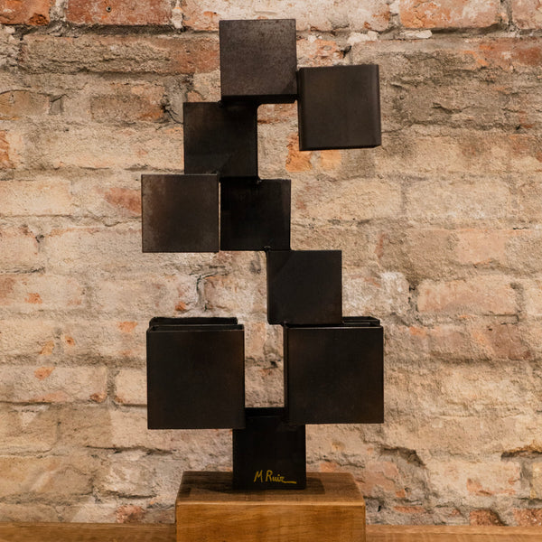 Escultura de cubos negros estilo multicúbico sobre base de madera