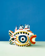 Jarrón de cerámica con forma de pez, vista lateral, pintura azul, amarilla y roja.