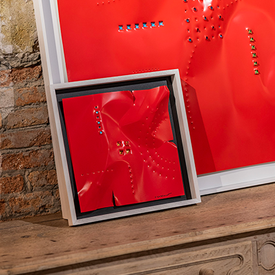 Cuadro de aluminio lacado rojo con relieve y tachuelas metálicas, en marco blanco