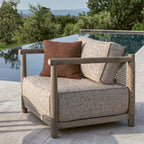 Butaca de teca natural con asiento beige y cojines marrón y gris claro