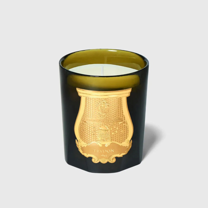 Vela en vaso negro con emblema dorado, cera blanca al ras y una mecha