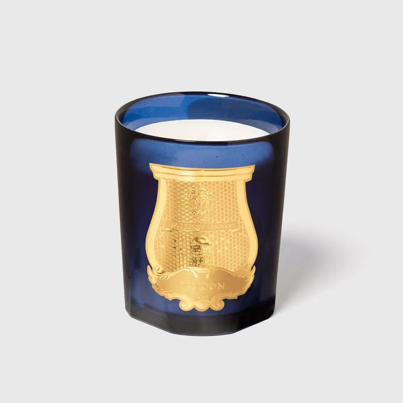 Vela en frasco de vidrio azul con mecha visible y motivos dorados grabados