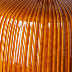 Detalle de base de vidrio ámbar acanalado, con reflejos y vetas verticales