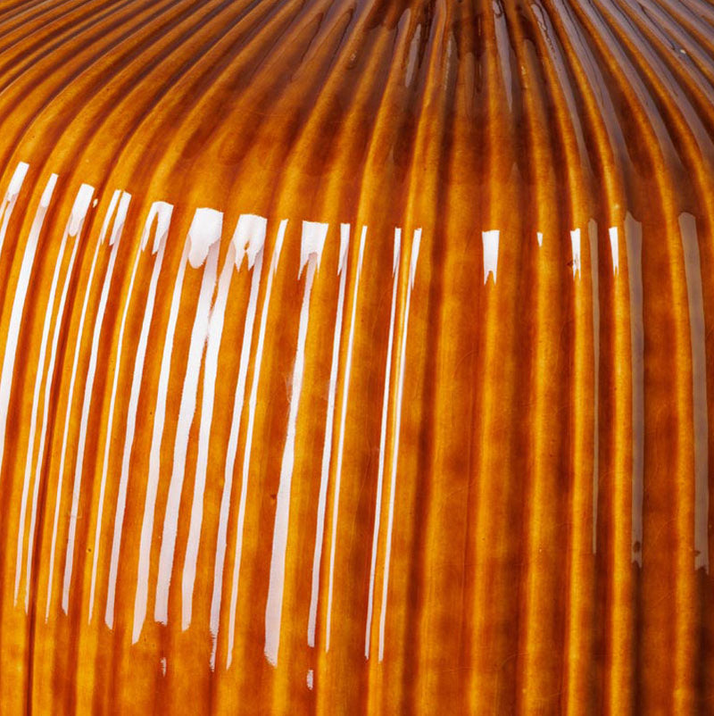 Detalle de base de vidrio ámbar acanalado, con reflejos y vetas verticales