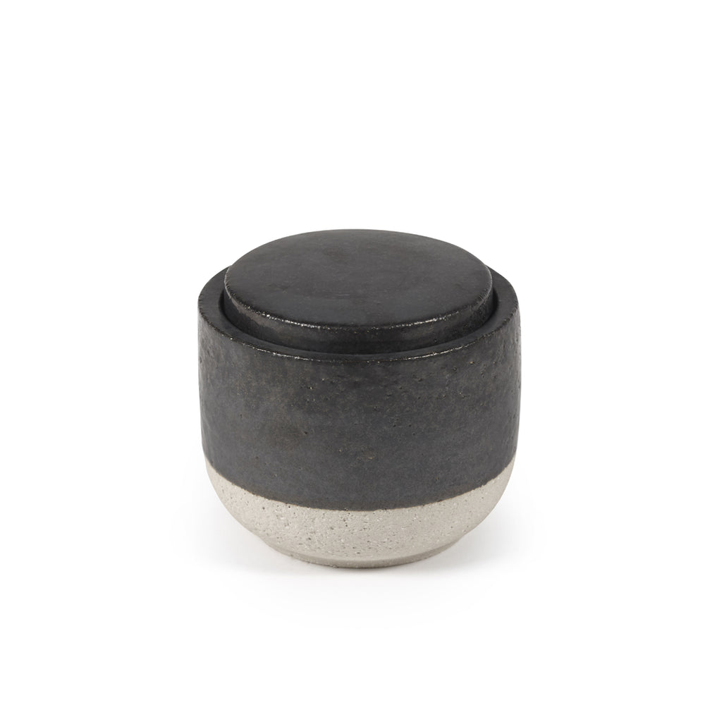 Vela perfumada decorativa en recipiente cilíndrico oscuro con tapa redonda negra