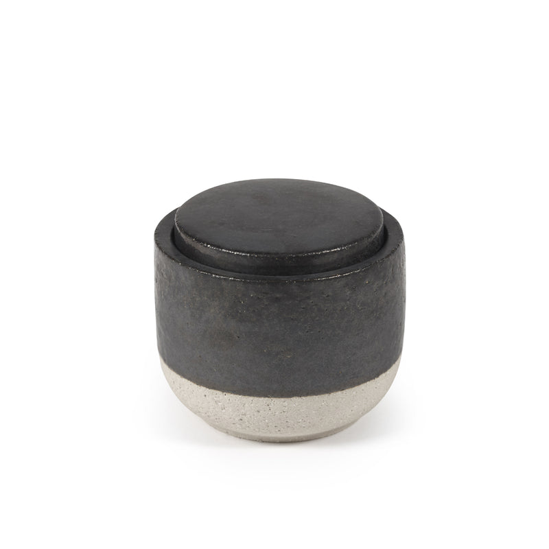Vela perfumada decorativa en recipiente cilíndrico oscuro con tapa redonda negra