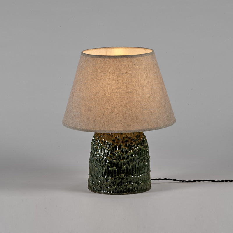 Lámpara de mesa con pantalla beige iluminada y base de tronco verde texturizado