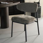 Silla tapizada gris jaspeado con respaldo oval y patas negras de metal.
