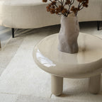 Mesa de centro redonda beige con sobre brillante y patas redondeadas, vista en ángulo.