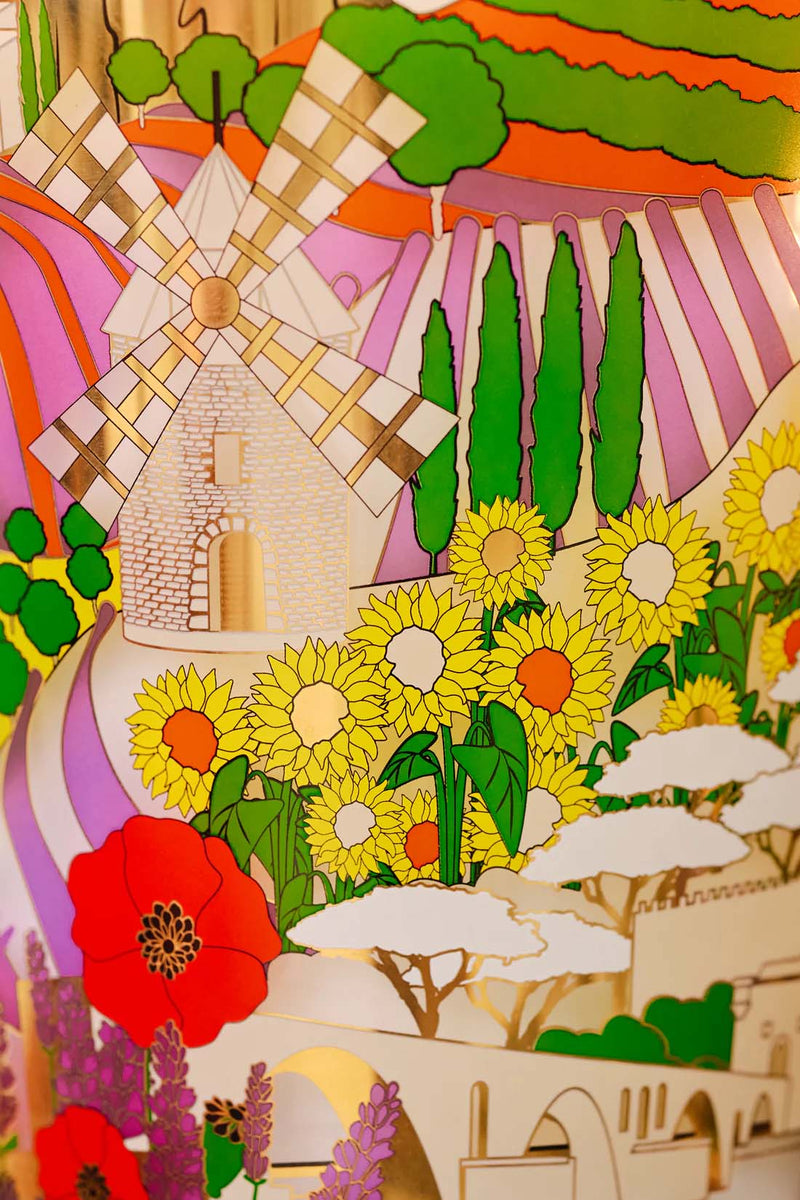 Difusor Provence: etiqueta con paisaje campestre y flores amarillas, verdes y rojas.