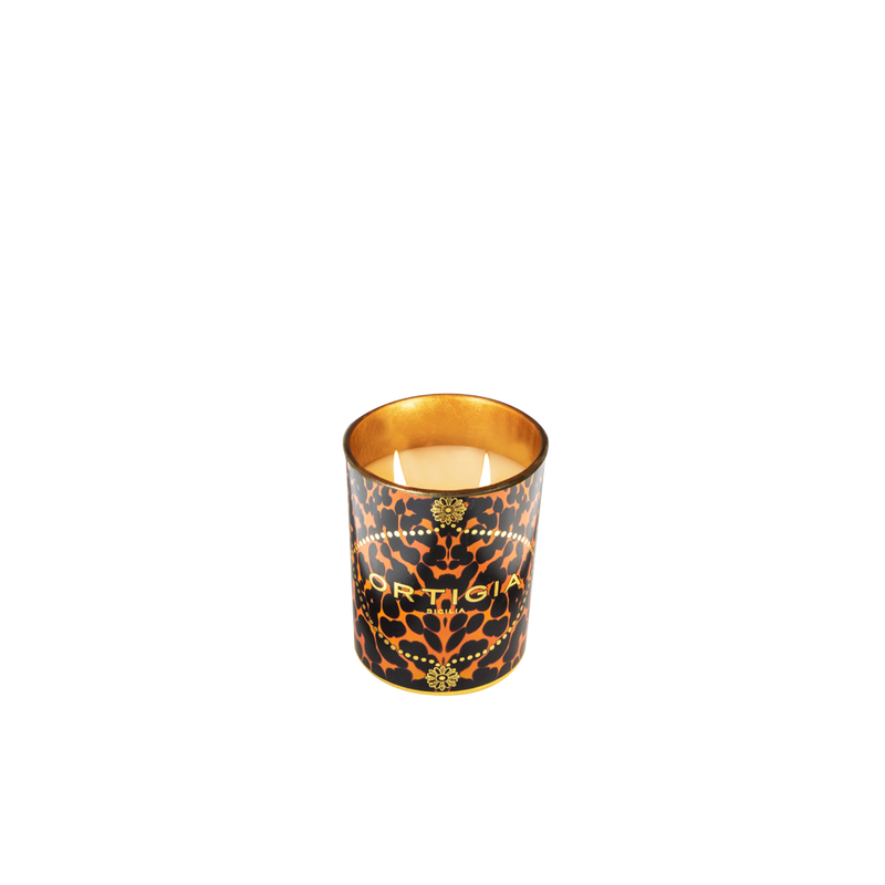 Vela perfumada Ortigia Ambra Nera encendida en vaso con estampado leopardo y flores doradas