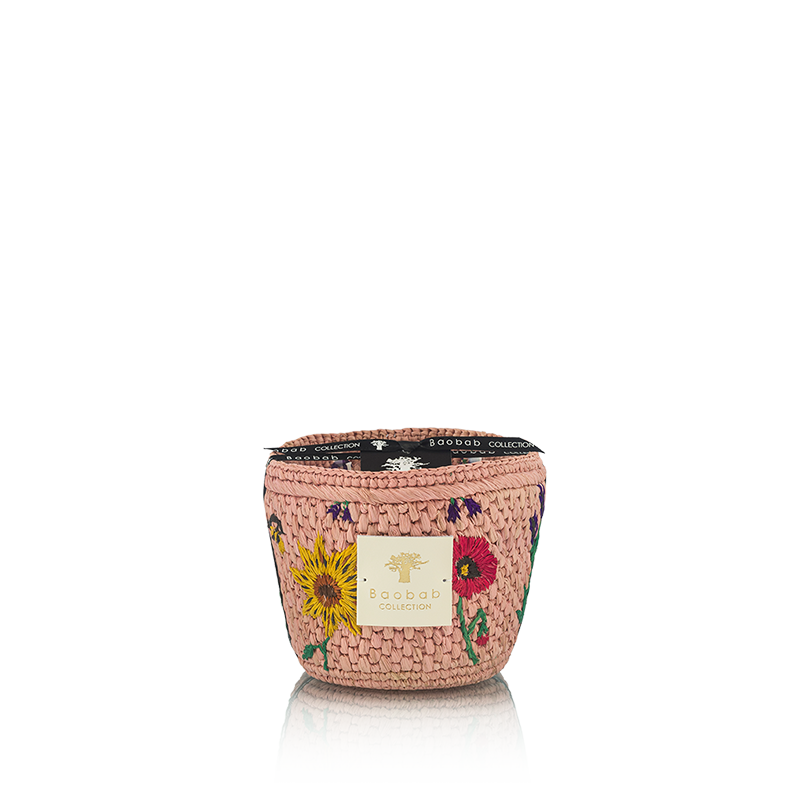 Vela en recipiente trenzado rosa con flores bordadas y etiqueta Baobab Collection en el frente.