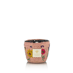 Vela en recipiente trenzado rosa con flores bordadas y tapa oscura alrededor del borde superior.