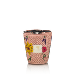 Vela en recipiente trenzado rosa con flores bordadas; etiqueta Baobab Collection y reflejo abajo.