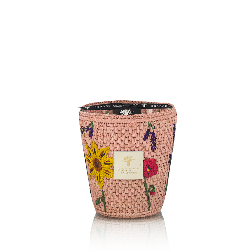 Vela en recipiente trenzado rosa con flores bordadas; etiqueta Baobab Collection y reflejo abajo.