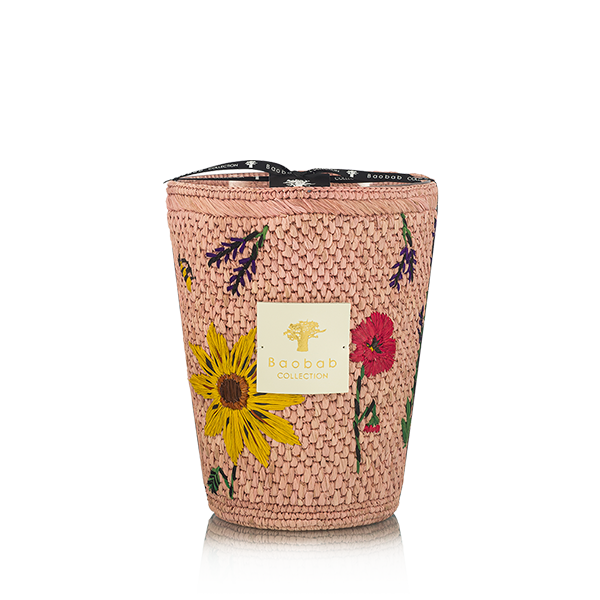 Vela en recipiente trenzado rosa con flores bordadas, etiqueta blanca y borde superior negro.