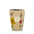 Vela en frasco de fibra tejida beige con flores amarillas y rojas, sobre fondo claro