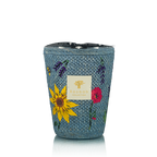 Vela en recipiente tejía azul con flores y etiqueta frontal, vista de frente