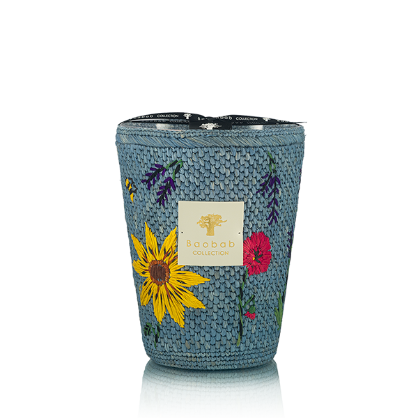Vela en recipiente tejía azul con flores y etiqueta frontal, vista de frente