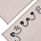 Esquina de individual beige con borde zigzag y bordado negro de flores y hojas