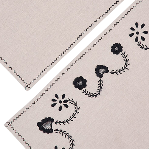 Esquina de individual beige con borde zigzag y bordado negro de flores y hojas