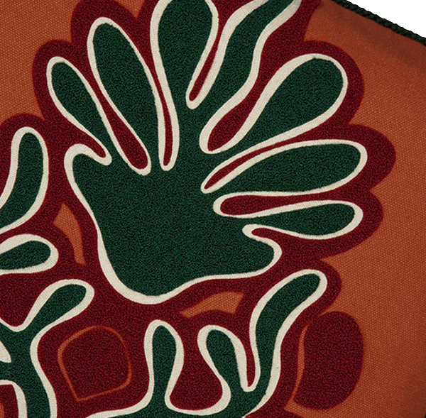 Cojín naranja con close-up del bordado de mano verde y contornos blancos