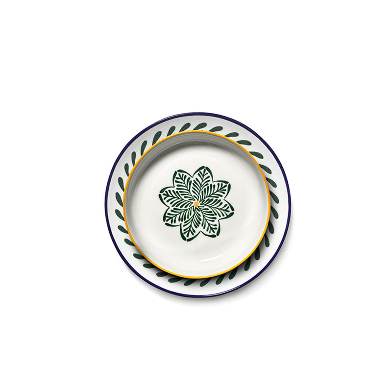 Plato cerámico blanco con borde amarillo y motivo verde sobre base azul con salpicaduras.