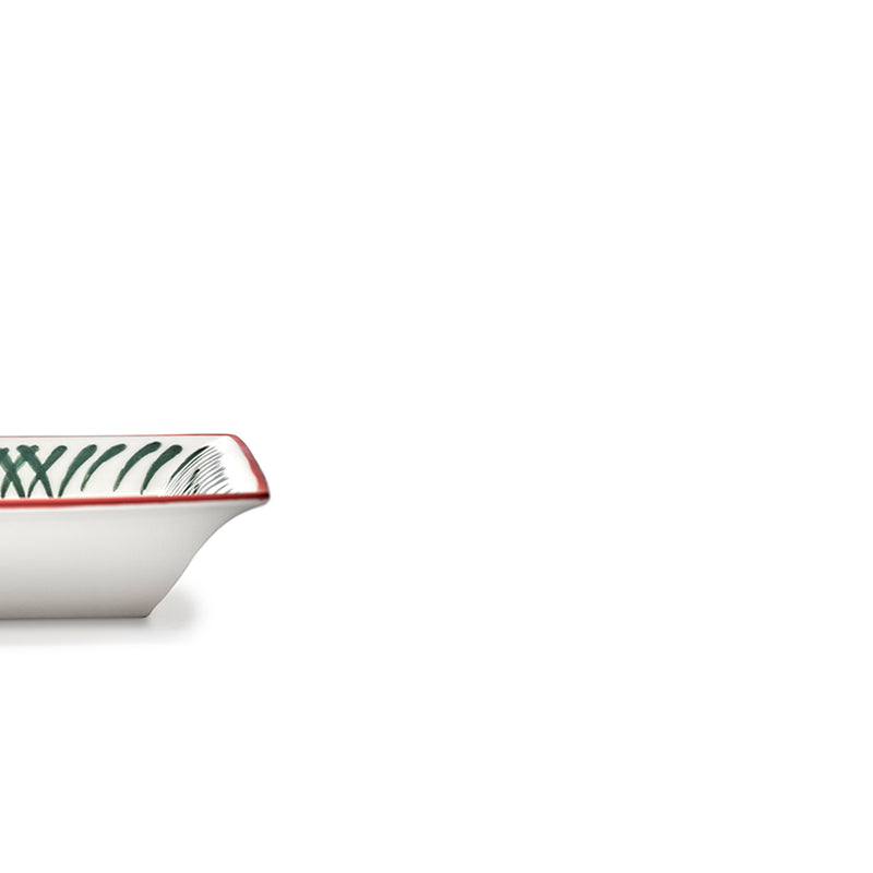 Esquina de plato rectangular cerámico con borde rojo y patrón verde y negro