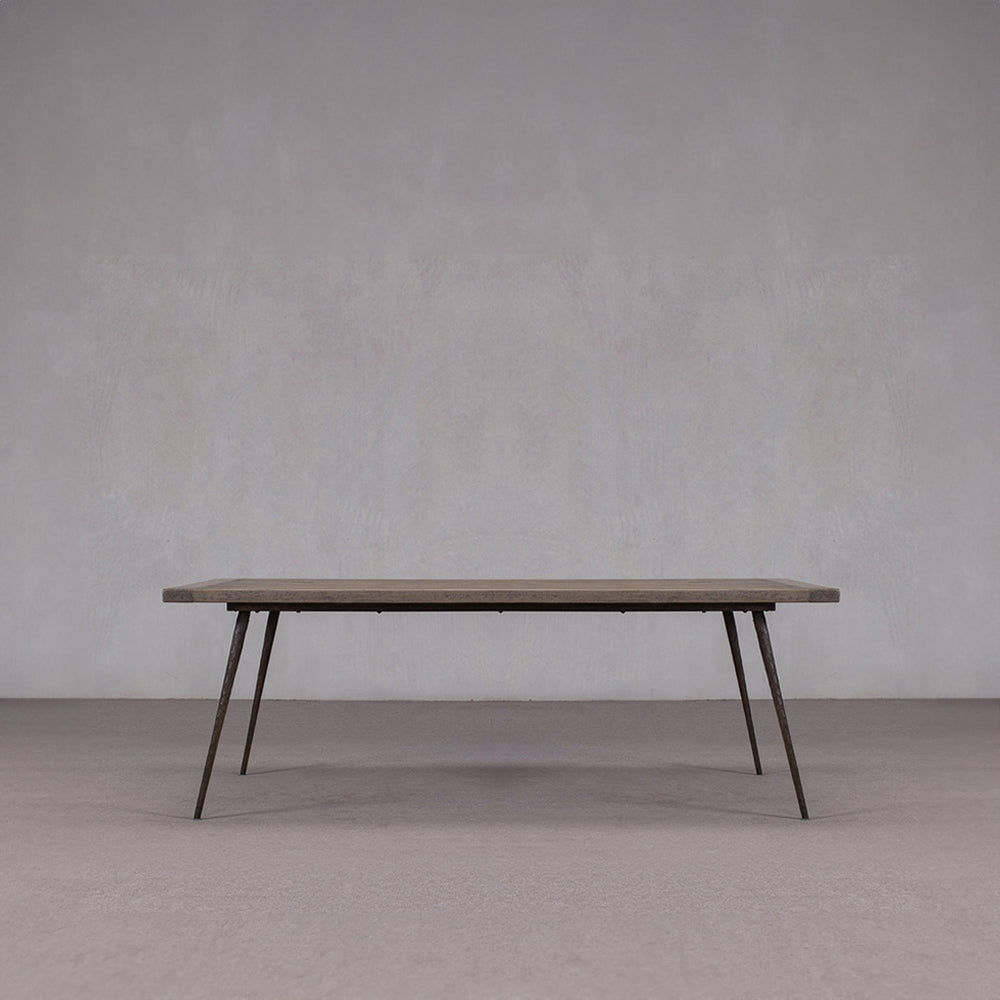 Mesa de comedor de madera con tablero rectangular oscuro y patas oblicuas de metal.