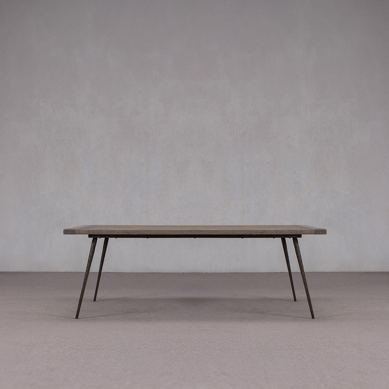 Mesa de comedor de madera con tablero rectangular oscuro y patas oblicuas de metal.