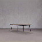 Mesa de comedor de madera con tablero rectangular oscuro y patas metálicas oblicuas.