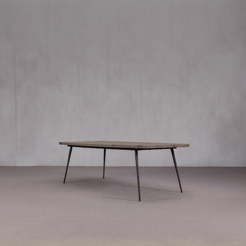 Mesa de comedor de madera con tablero rectangular oscuro y patas metálicas oblicuas.