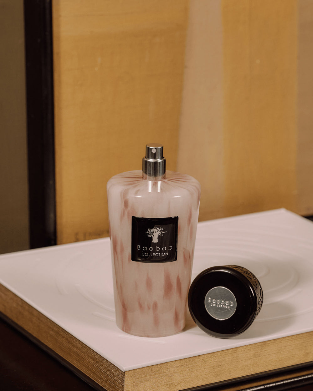 Ambientador en spray Baobab Collection White Pearls, frasco de vidrio rosado con tapa negra al lado.