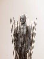 Escultura de busto con varillas metálicas y rostro de piedra gris, vista frontal