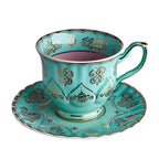 Taza de té turquesa con interior rosa, motivos decorativos y asa verde en platillo