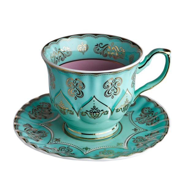 Taza de té turquesa con interior rosa, motivos decorativos y asa verde en platillo