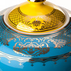 Tapa dorada de tetera azul con motivos ornamentales en amarillo y crema