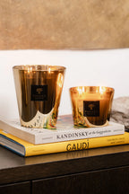 Par de velas en vasos de vidrio dorado con llamas y etiqueta Baobab.