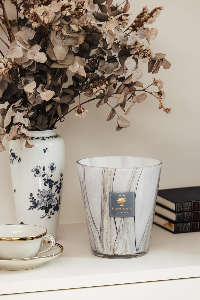 Vela en vaso de vidrio con vetas grises y etiqueta azul Baobab Collection, sobre mesa