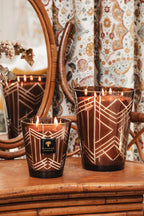 Velas en vasos de vidrio ahumado con patrón geométrico dorado y llama encendida