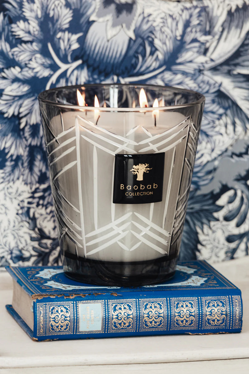 Vela encendida en vaso de vidrio ahumado con patrón blanco y etiqueta Baobab Collection