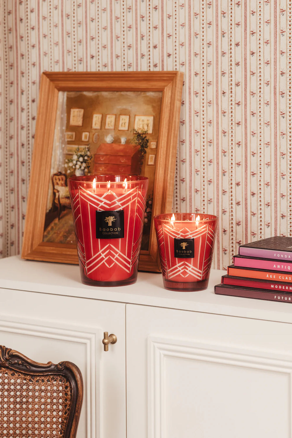 Vela en vaso de vidrio rojo con líneas blancas y etiqueta Baobab Collection, encendida