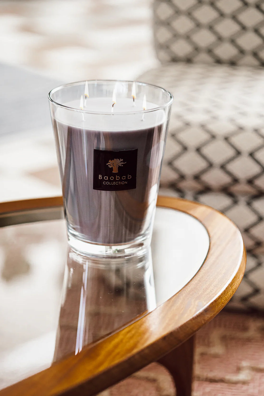 Vela en vaso de vidrio con cera morada y mechas encendidas, etiqueta Baobab