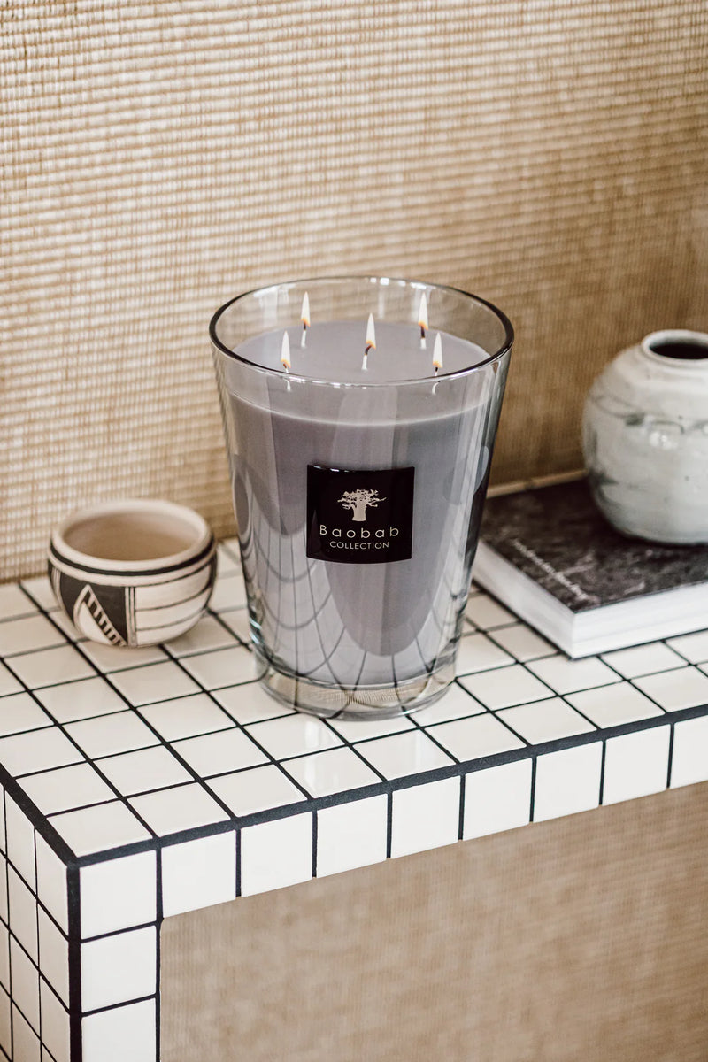 Vela en vaso de vidrio con cera morada y mechas encendidas, etiqueta Baobab