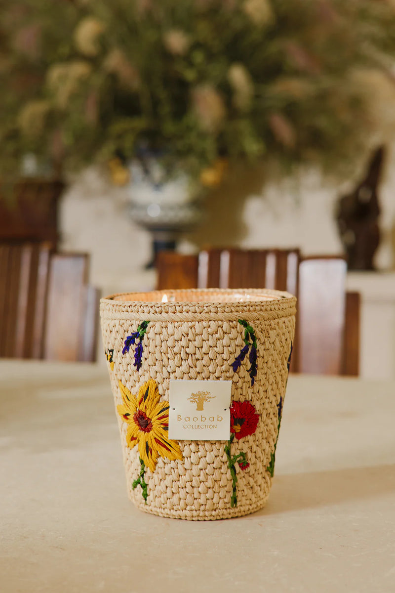 Vela en frasco de fibra tejida beige con flores amarillas y etiqueta frontal