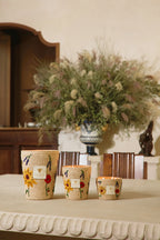 Set de velas en frascos de fibra tejida con estampado floral, sobre mesa