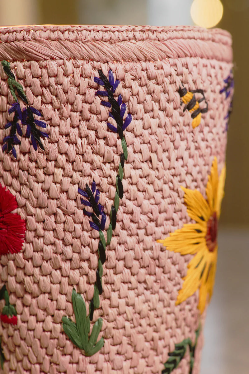Vela en recipiente trenzado rosa con detalle de flores bordadas y textura del tejido.