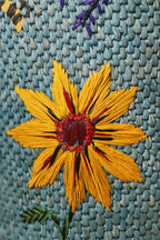 Detalle de vela: flor amarilla bordada sobre recipiente tejía azul